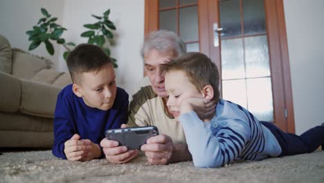 senior and children holding mobile phone. attentive granddad with children pointing finger in mobile, communication and technology concept