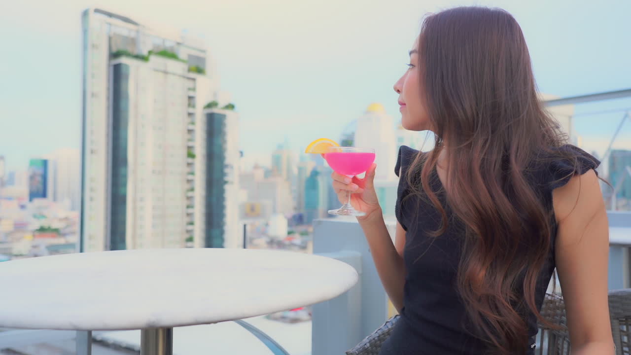 Against the backdrop of a modern urban skyline, a gorgeous woman sips from an exotic cocktail