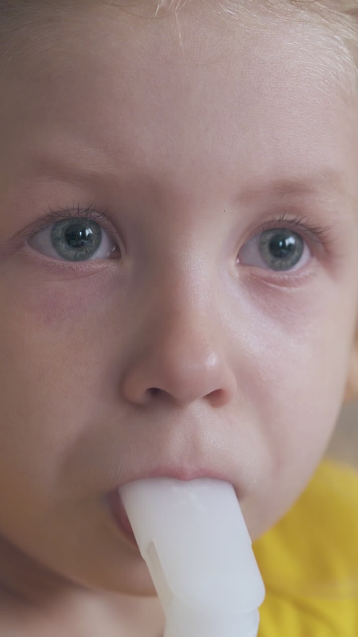 unhappy blue eyed small girl uses modern inhaler in light room on blurred background extreme close view