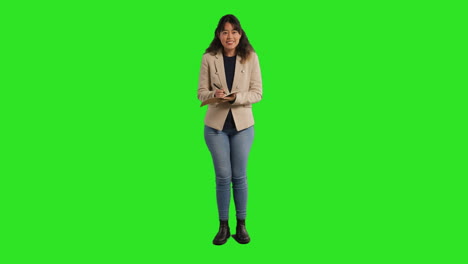 Full-Length-Studio-Portrait-Of-Female-Teacher-With-Notebook-Talking-To-Class-Standing-Against-Green-Screen