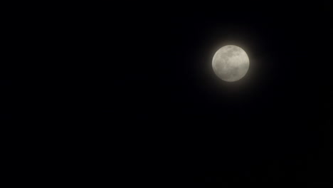 nubes negras pasando frente a una luna llena en el cielo nocturno