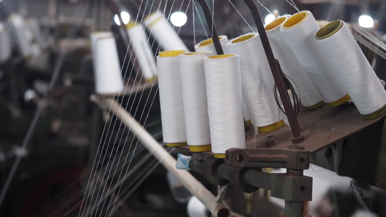 Close-up view of thread spools on textile machinery in a factory.