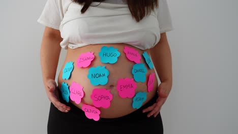 pregnant belly with sticky notes of baby names, woman hesitating with raised arms