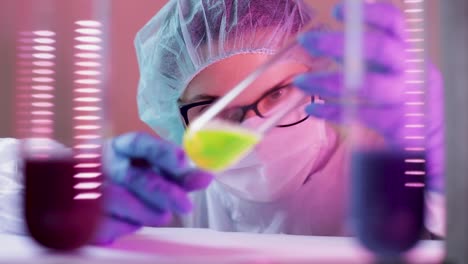 scientist woman shaking glass tube with yellow liquid solution and taking notes on reaction of coronavirus analysis