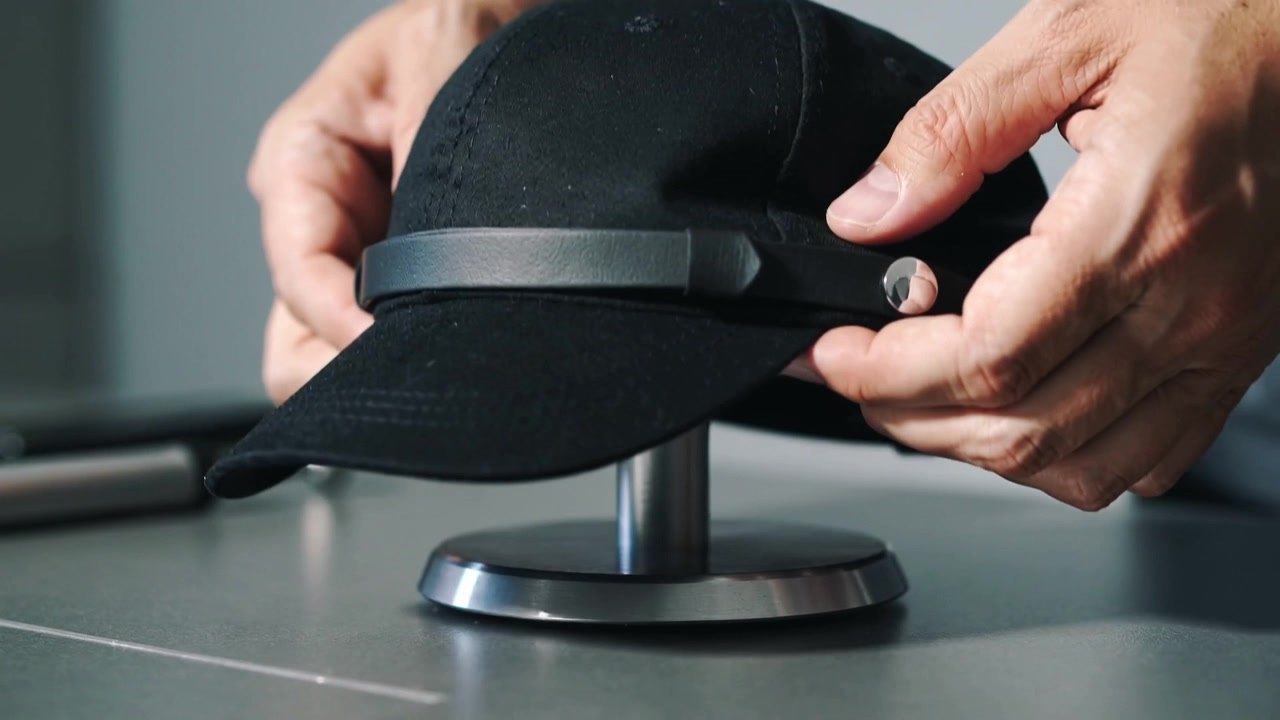Adjusting hands placing black baseball cap on metal stand on table, with strap, snap, torch, sleeve