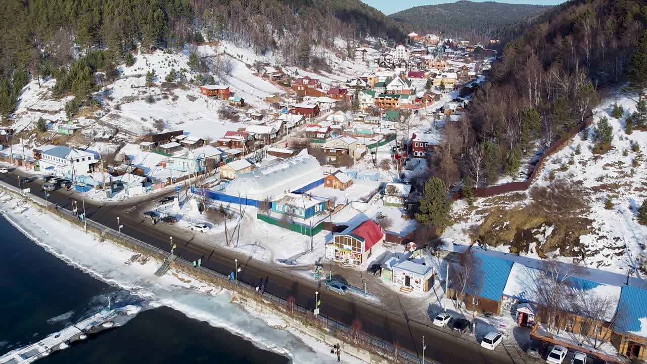 Witness the stunning frozen landscape of Lake Baikal in Siberia, showcasing a picturesque jetty and the tranquil charm of winter in the surrounding town. Nature captivates with its icy beauty.