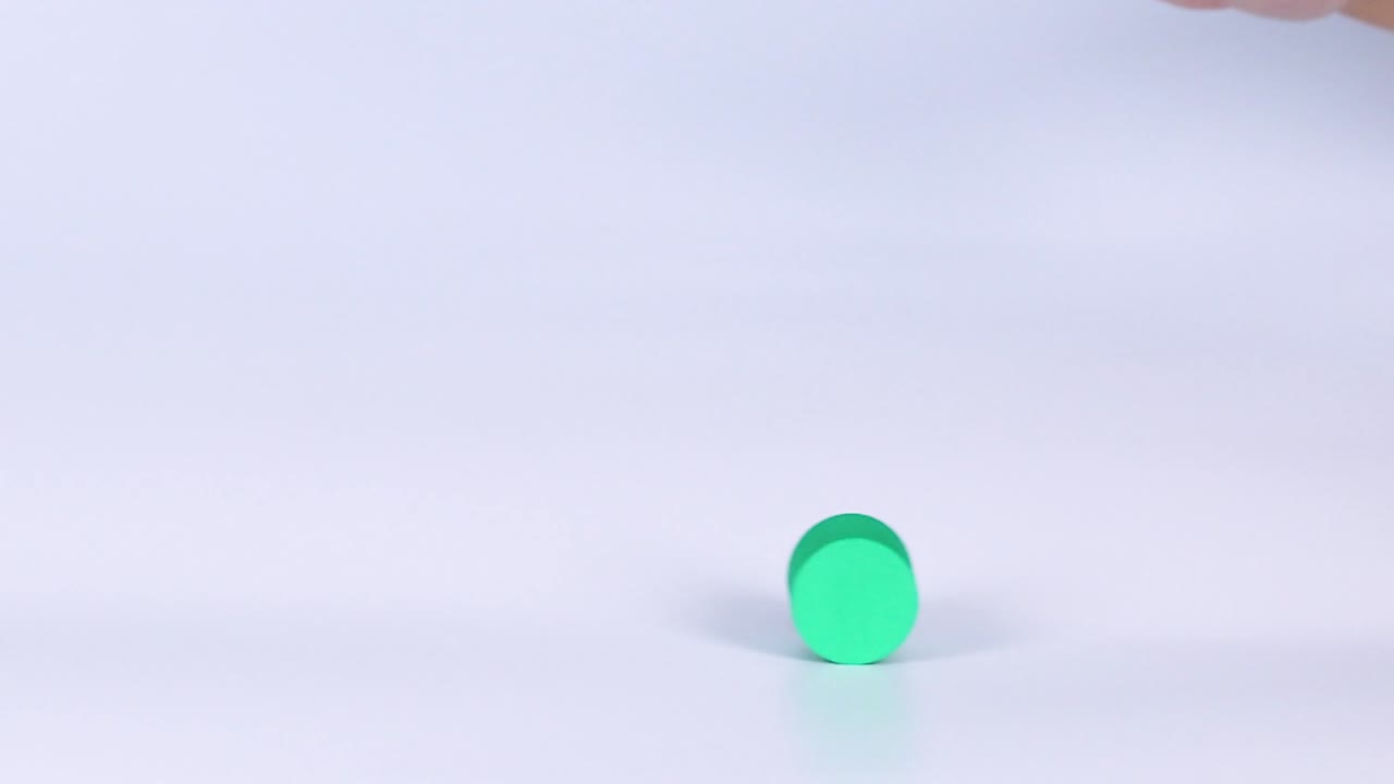 A hand reaches towards and interacts with a small green cylindrical object on a white surface.