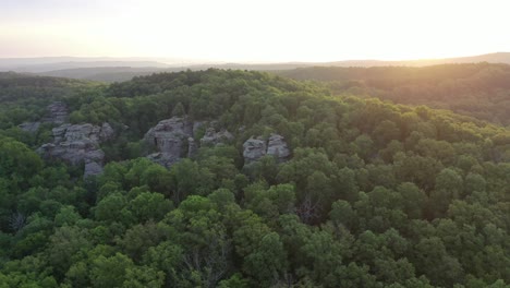 rocky cliff covered in lush forest trees with sunrise in horizon, aerial view