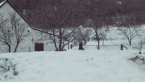 little girl falls while carrying wooden sled to top of hill in snowy landscape