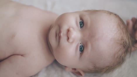 infant son with big blue eyes and fair hair looks at camera