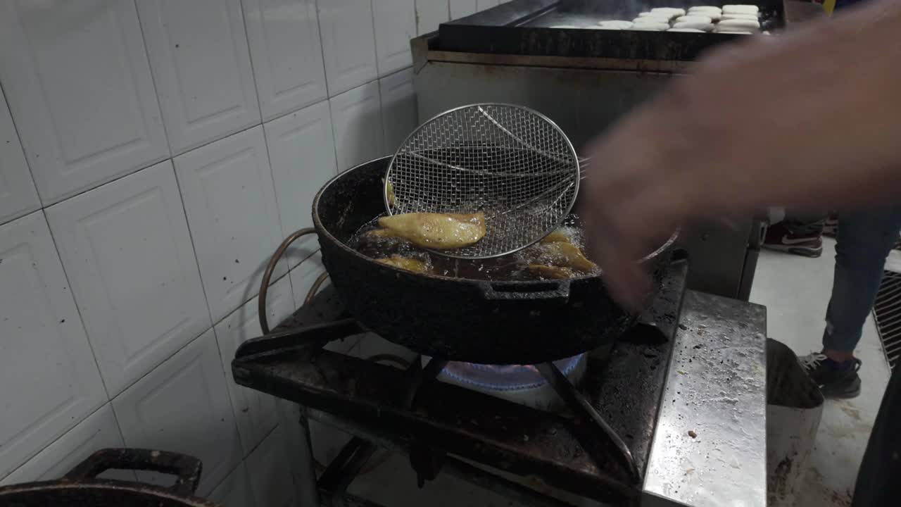 handheld view of golden empanadas being retrieved from sizzling hot oil, highlighting the intense cooking process., traditional Latin food