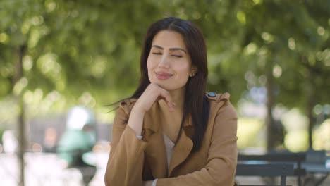 Portrait-Of-Smiling-Muslim-Woman-Sitting-At-Outdoor-Table-On-City-Street