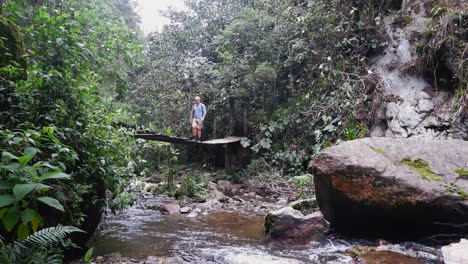 Male-hiker-crosses-narrow-jungle-river-on-sketchy-suspension-bridge