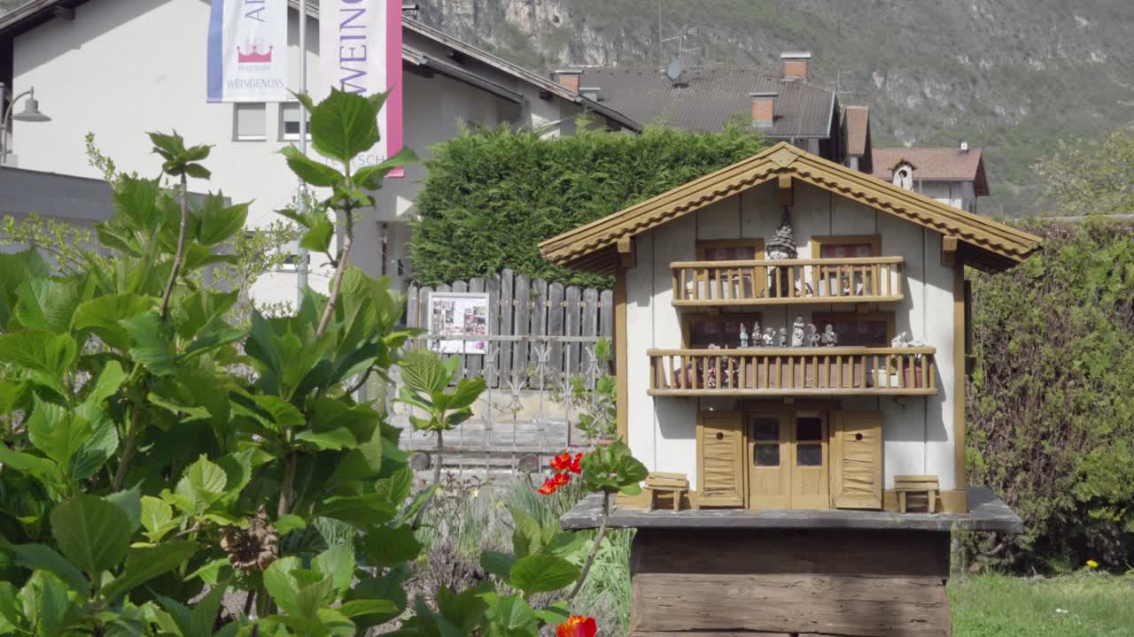 A model house stands in a garden. A lizard is running around under the house.