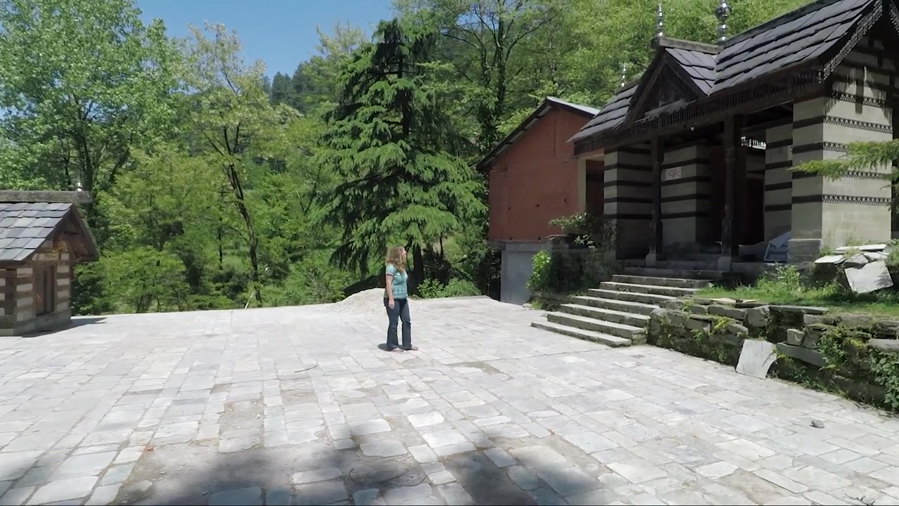 ヒマラヤの寺院を出る美しい女性。広角サイドショット。彼女は柱を通り過ぎて祭壇へ向かう。安定したトラッキングショット。