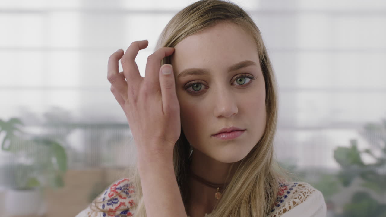 사무실 작업 공간 배경에서 머리카락을 통해 손을 실행하는 카메라를보고 있는 아름다운 젊은 금발 여성 인턴의 포트레이트