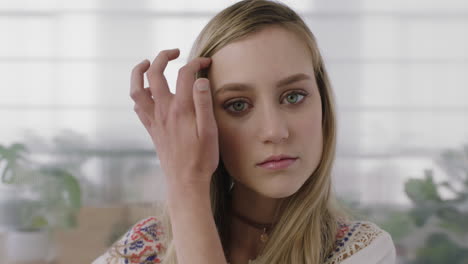 close-up-portrait-of-beautiful-young-blonde-woman-intern-looking-at-camera-running-hand-through-hair-in-office-workspace-background