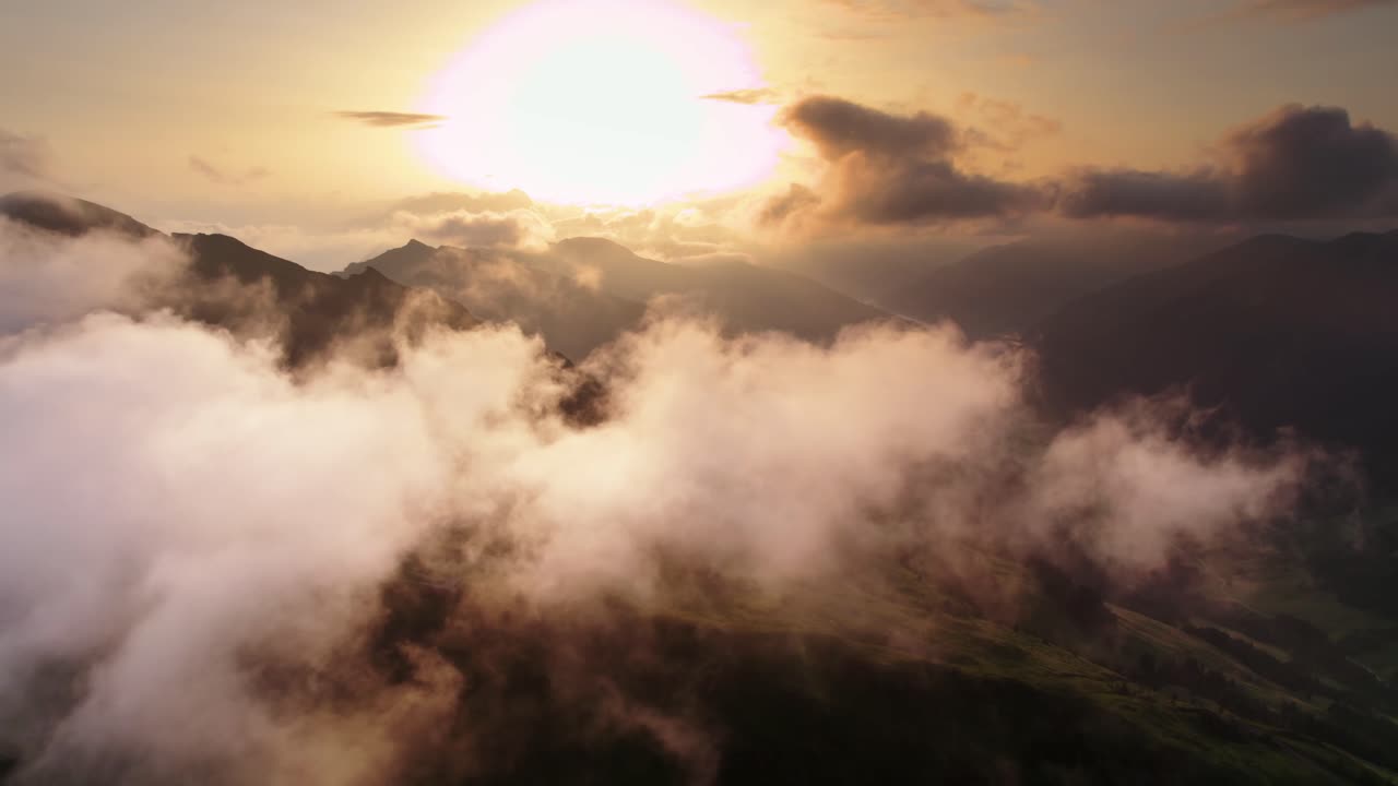 droneshot volando por encima y a través de las nubes liberando la vista de la cordillera y los valles en austria con el sol muy bajo