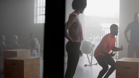 diverse group fitness class watching male coach jump onto box, cross training at gym, in slow motion