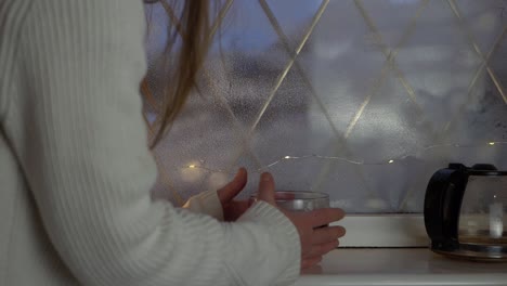 mujer calentándose las manos en una taza de café recién hecho en la ventana de tiro medio