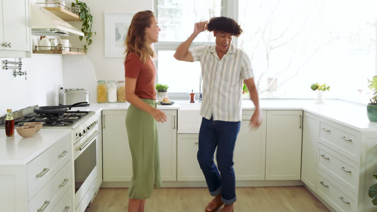 Diverse couple dancing joyfully in bright kitchen, enjoying fun moment together, at home