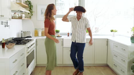 diverse couple dancing joyfully in bright kitchen, enjoying fun moment together, at home