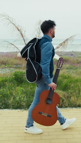 man walking with his guitar in hand on the sidewalk near the sea