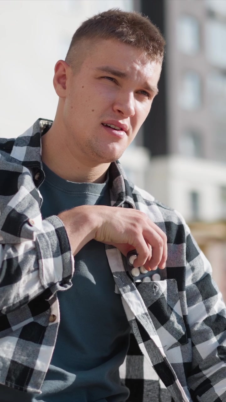 Close up of young man wearing casual clothing including checkered shirt and blue t shirt in various poses. Soft natural light highlights his facial features as man looks down or adjusts