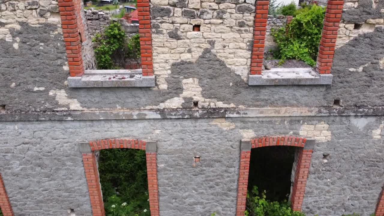 Cinematisk nærbillede med drone, der tilter op af Karpero jernbanestations facade i Grevena, Grækenland. Detaljeret udsigt over stenmurer fra 1930'erne og vinduesbuer i røde mursten. Ideel til historie- og urbex-film