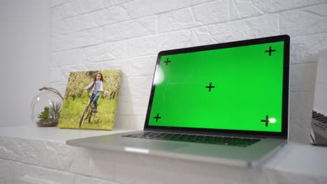 green screen laptop computer sitting on a home work desk next to a desk lamp.