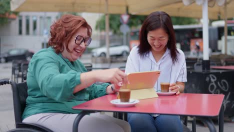 two women at outdoor cafe with coffee and tablet