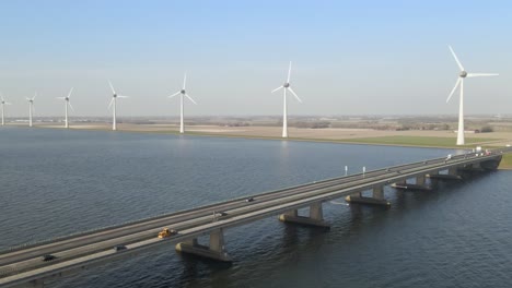 Aerial-view-cars-crossing-bridge-over-water,-windpark-in-background,-sustainable-energy-concept