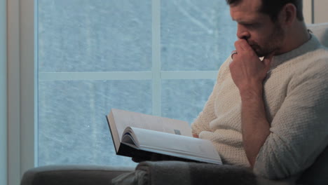 disparo lateral de un hombre leyendo un libro por la ventana durante una tormenta de nieve