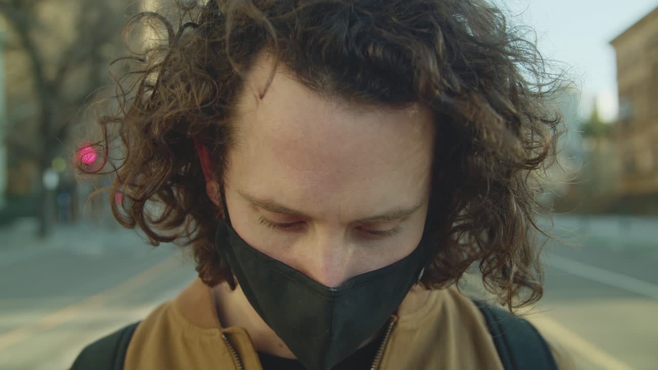 Man wearing a mask looking down on a city street during a quiet afternoon in an urban environment