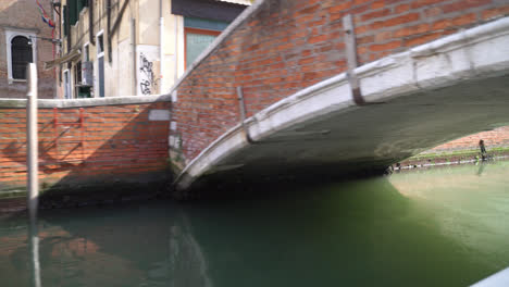 pov from a boat cruising in the canal passing under the stone bridge in venice, italy