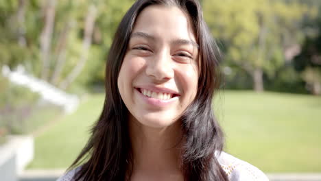 Retrato-De-Una-Feliz-Adolescente-Birracial-Sonriendo-En-Un-Jardín-Soleado,-Cámara-Lenta