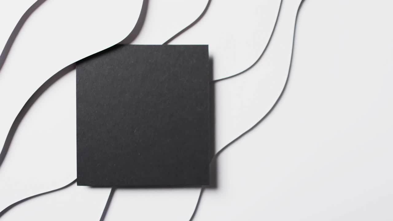 Vídeo em close-up de quadrado de papel preto com recortes em formato de ondas e espaço para texto em fundo branco