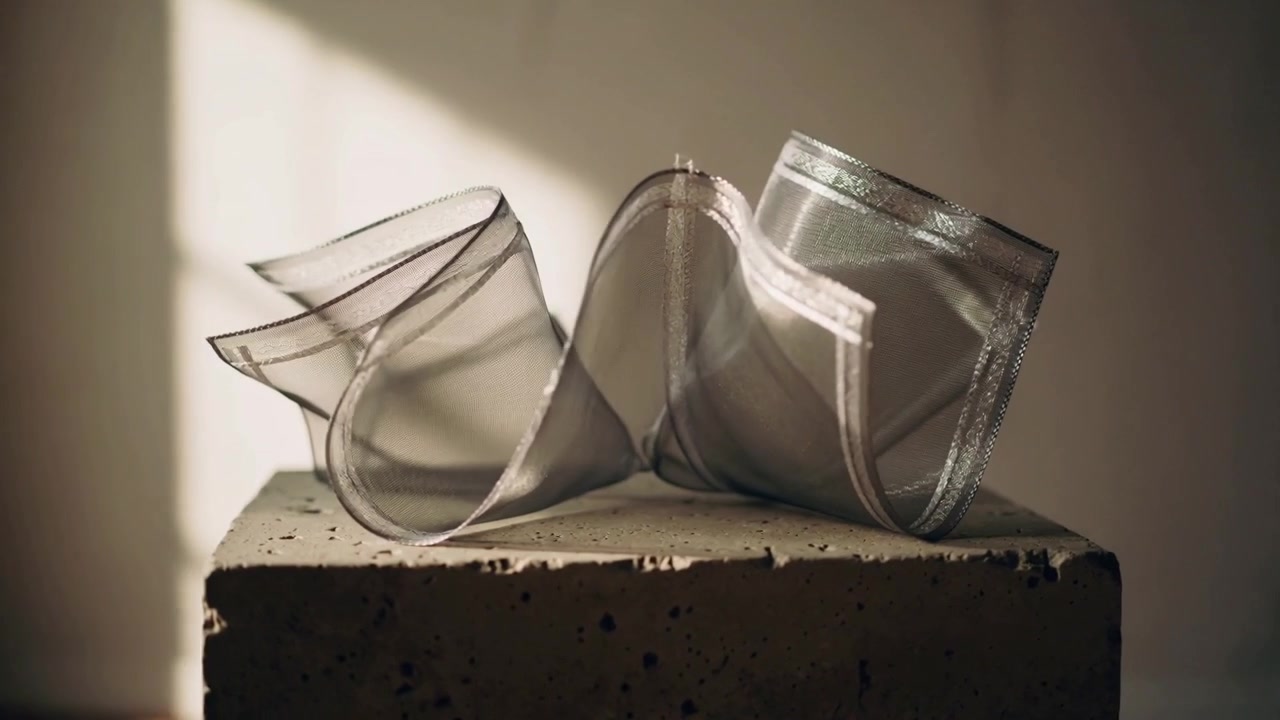 Sunbeam shifting, translucent silver organza lifting and unfurling on concrete plinth