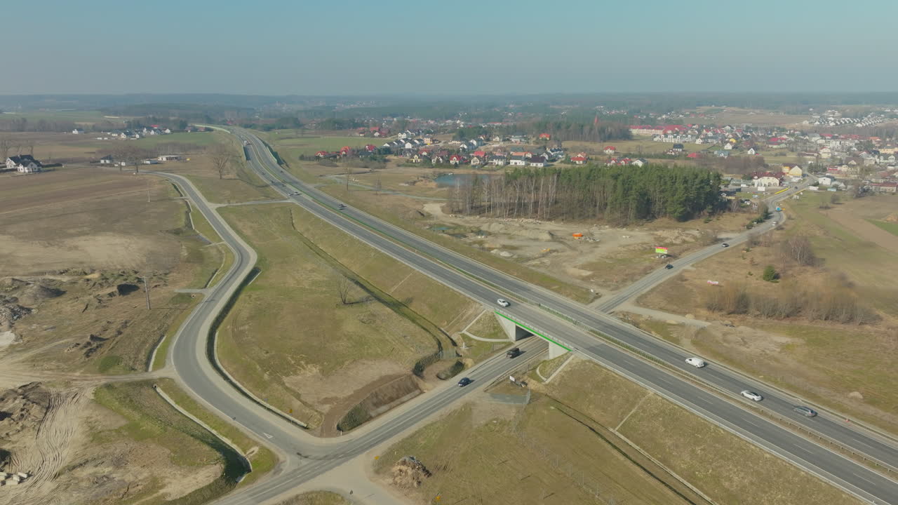 vista aérea de una autopista moderna, coches en movimiento en la carretera abierta en medio de un paisaje rural, y un complejo sistema de intercambio de carreteras con carriles que se fusionan y divergen