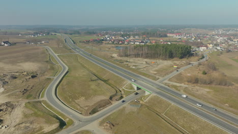 vista aérea de una autopista moderna, coches en movimiento en la carretera abierta en medio de un paisaje rural, y un complejo sistema de intercambio de carreteras con carriles que se fusionan y divergen