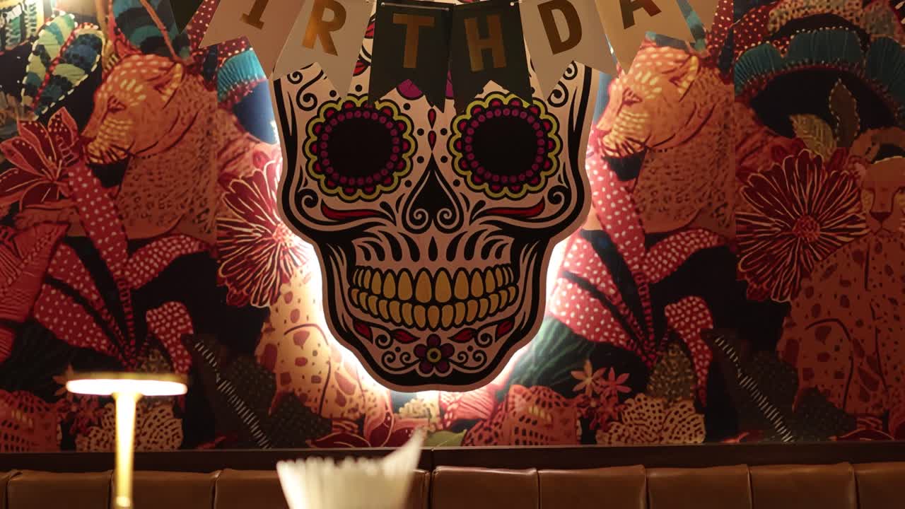 A colorful skull-themed birthday setup with festive decorations and balloons in a dimly lit Bangkok restaurant