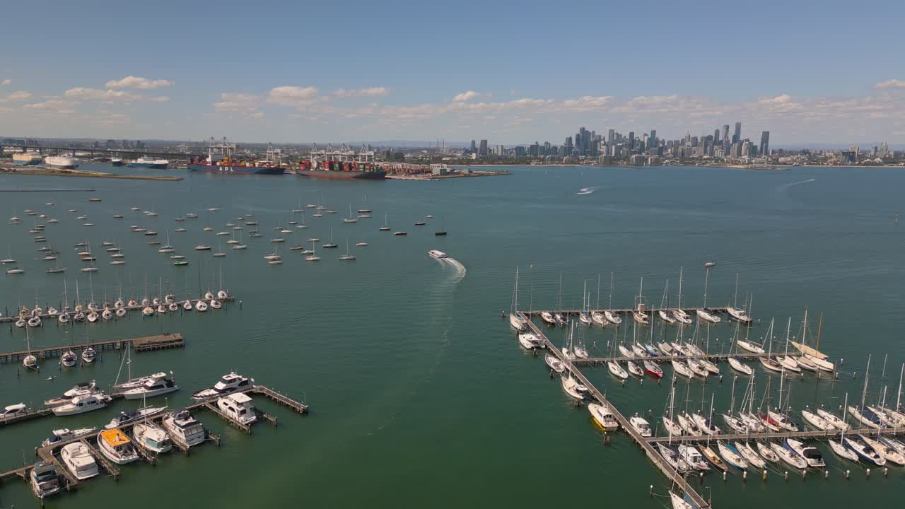 Drone footage panning towards Melbourne City from Gem Pier in Williamstown. Rows of ships can be seen docked along the pier.