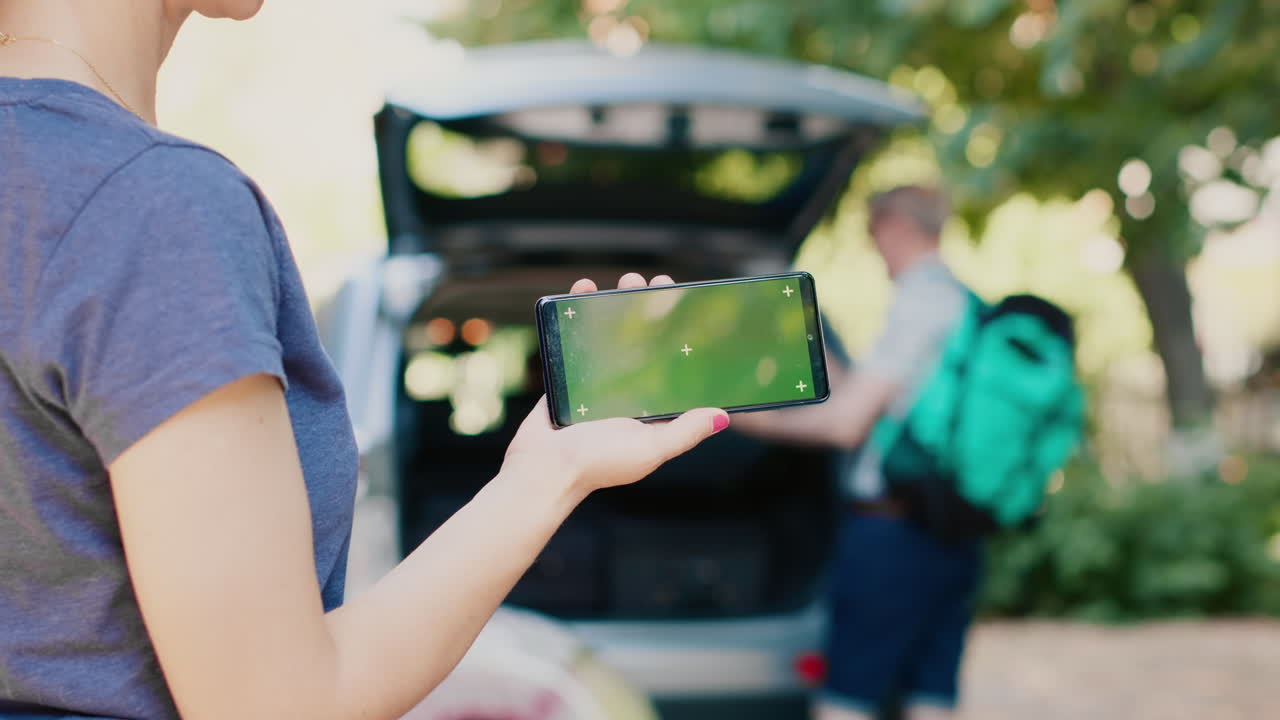 A woman holding a phone with a green screen in front of a car