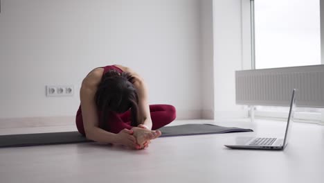 mujer deportiva haciendo ejercicios de estiramiento en la alfombra de yoga mientras ve un video de fitness en línea en una computadora portátil