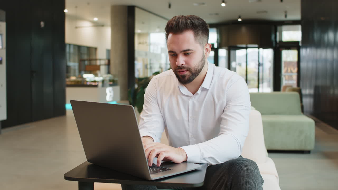 Disappointed businessman feeling overeating during work process on laptop in modern office lobby