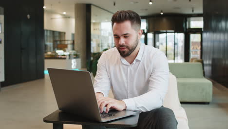 disappointed businessman feeling overeating during work process on laptop in modern office lobby