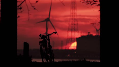 a bicycle silhouetted at sunset with wind turbines and industrial skyline in the background