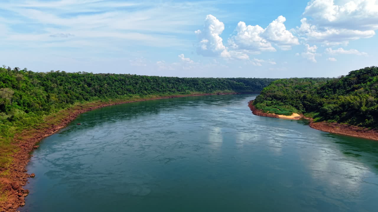 Paraná River flowing between Paraguay and Argentina—lush forest banks, red soil, and sandy curves frame the natural border in a calm, expansive drone establishing shot