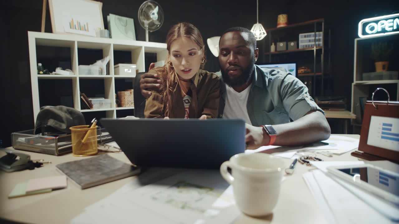 Flirting mixed race couple talking about data on laptop screen screen in office.