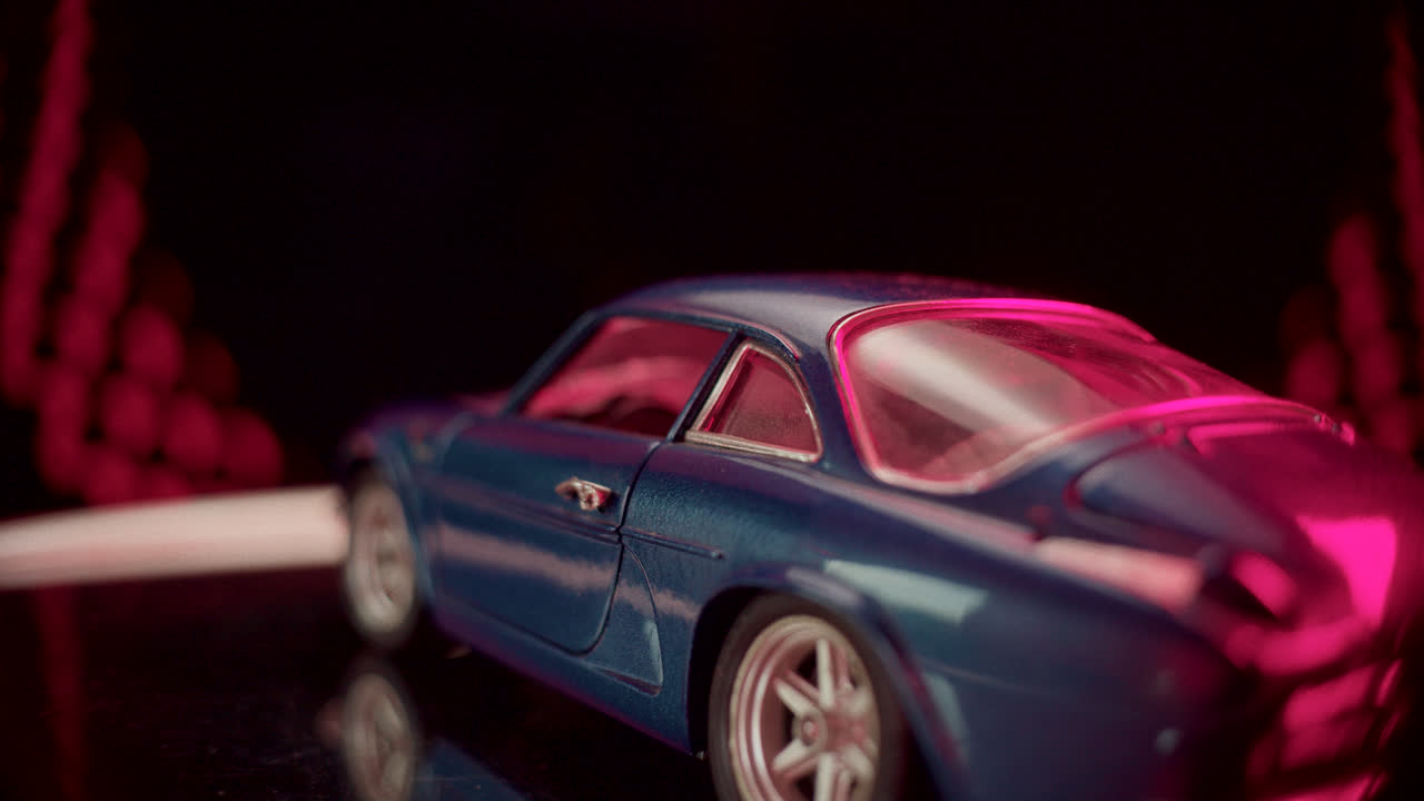 A detailed close-up of a blue model car illuminated by vibrant pink light